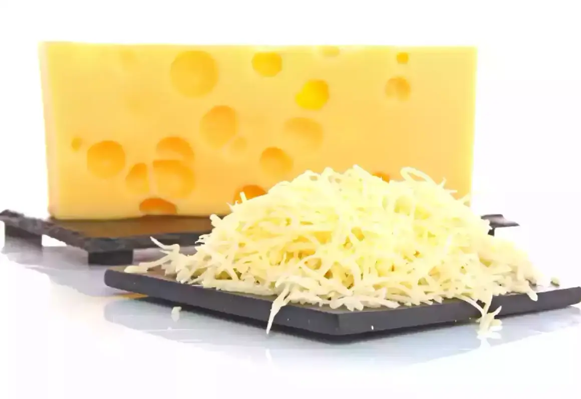 Bloque de queso suizo con agujeros y una pila de queso rallado, listo para ser queso que se derrite.