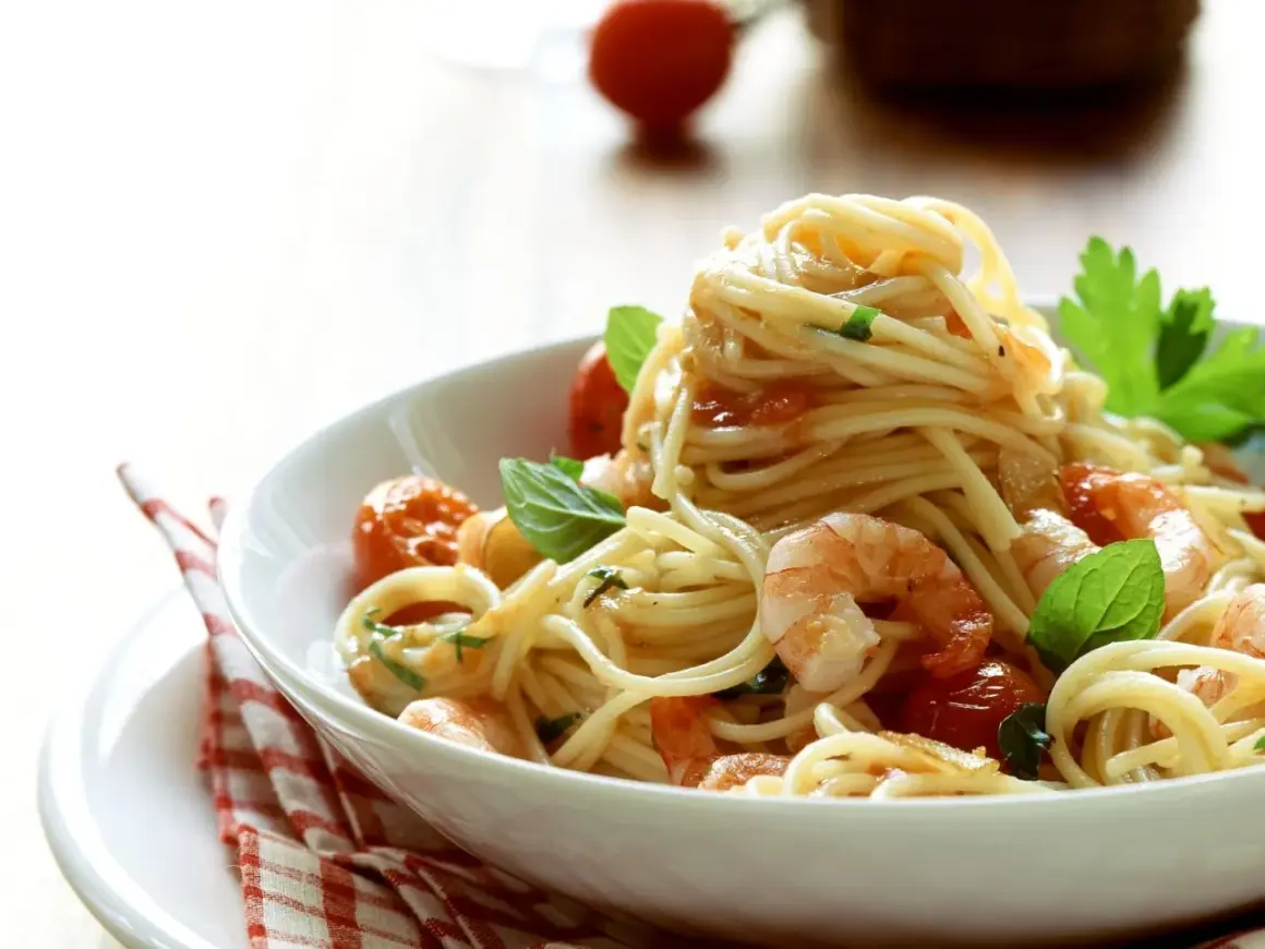 Ein Teller mit köstlichen Spaghetti mit Garnelen, Kirschtomaten und frischem Basilikum, appetitlich angerichtet.