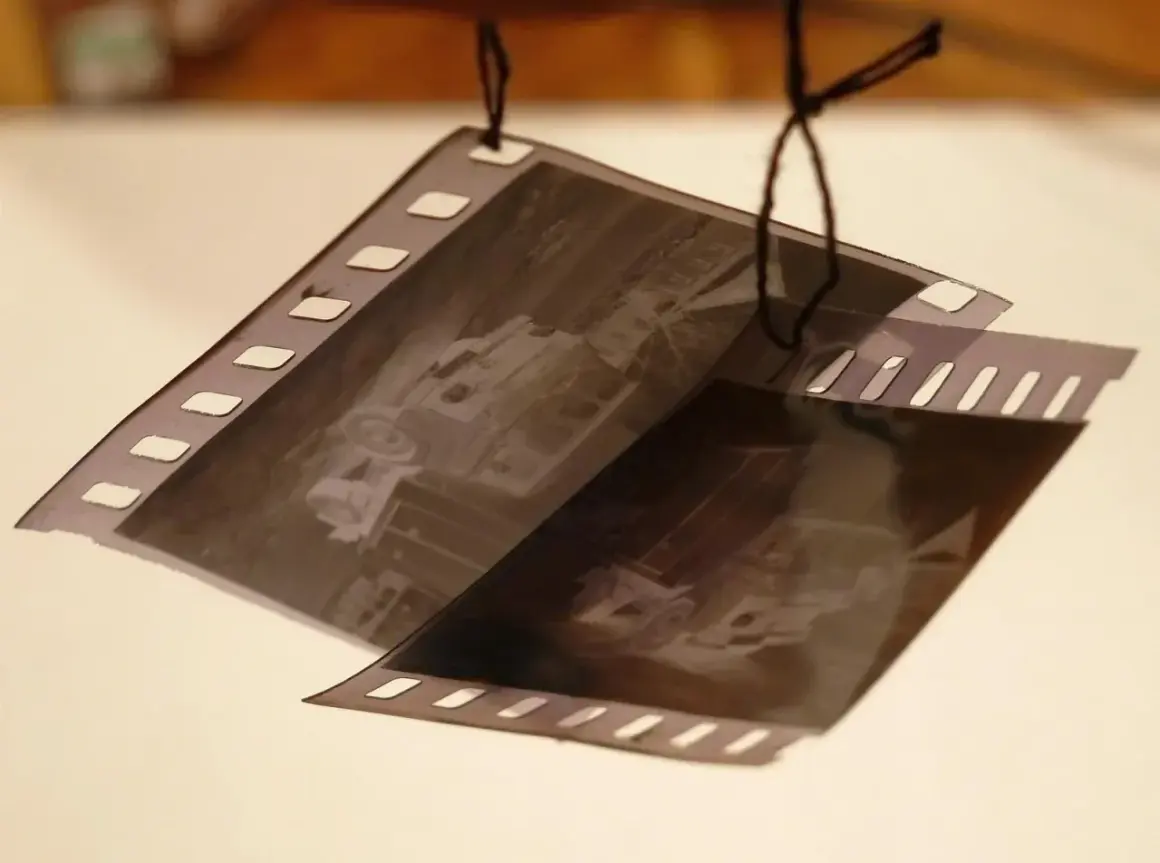 Klisze filmowe wiszą na sznurku, czekając na wywołanie. Zdjęcia przedstawiają stare samochody.