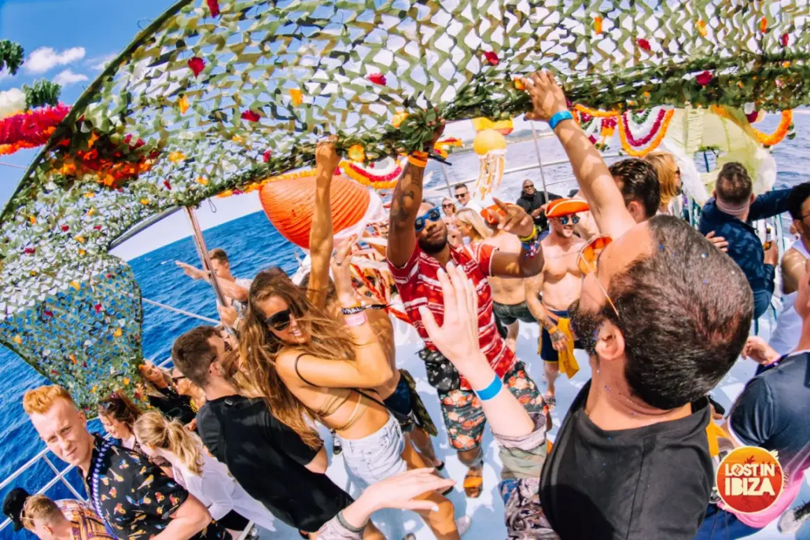 Festa in barca con gente che balla sotto una rete decorata. James Jones DJ anima la folla con la sua musica.