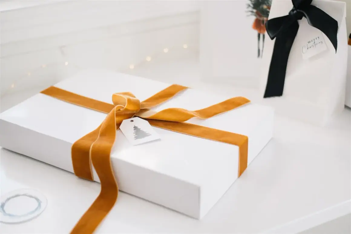 Ett vitt paket med gyllene sammetsband, ett sätt att slå in paket utan tejp. En julklapp med en liten etikett med gran.