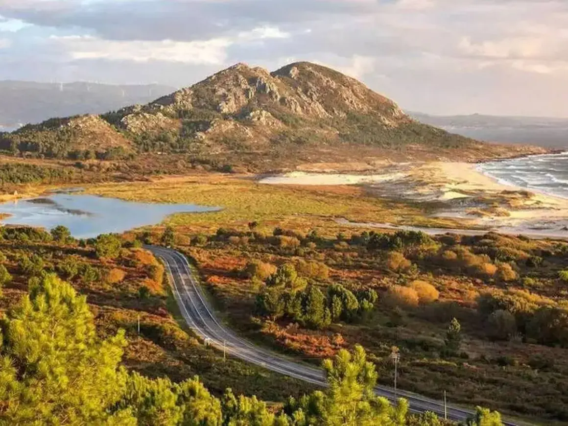 Carretera serpenteante hacia el monte Louro, con un lago, dunas y el mar al fondo.