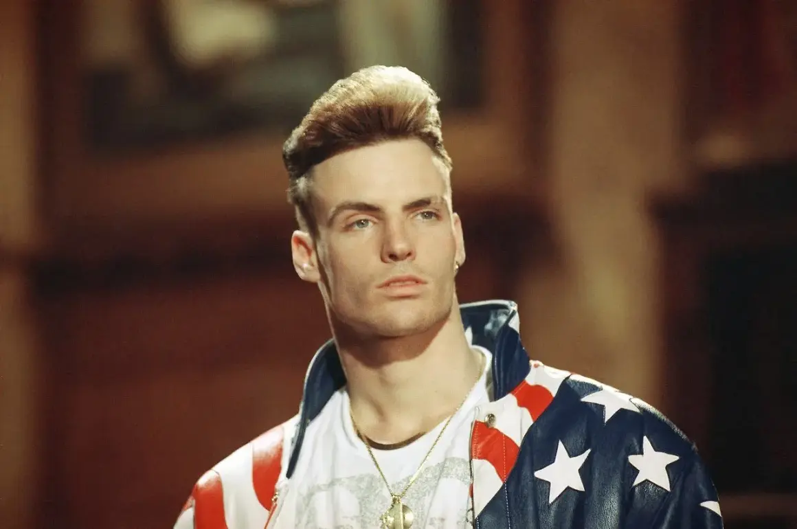 Homme blond avec une coiffure audacieuse, portant une veste aux couleurs du drapeau américain.