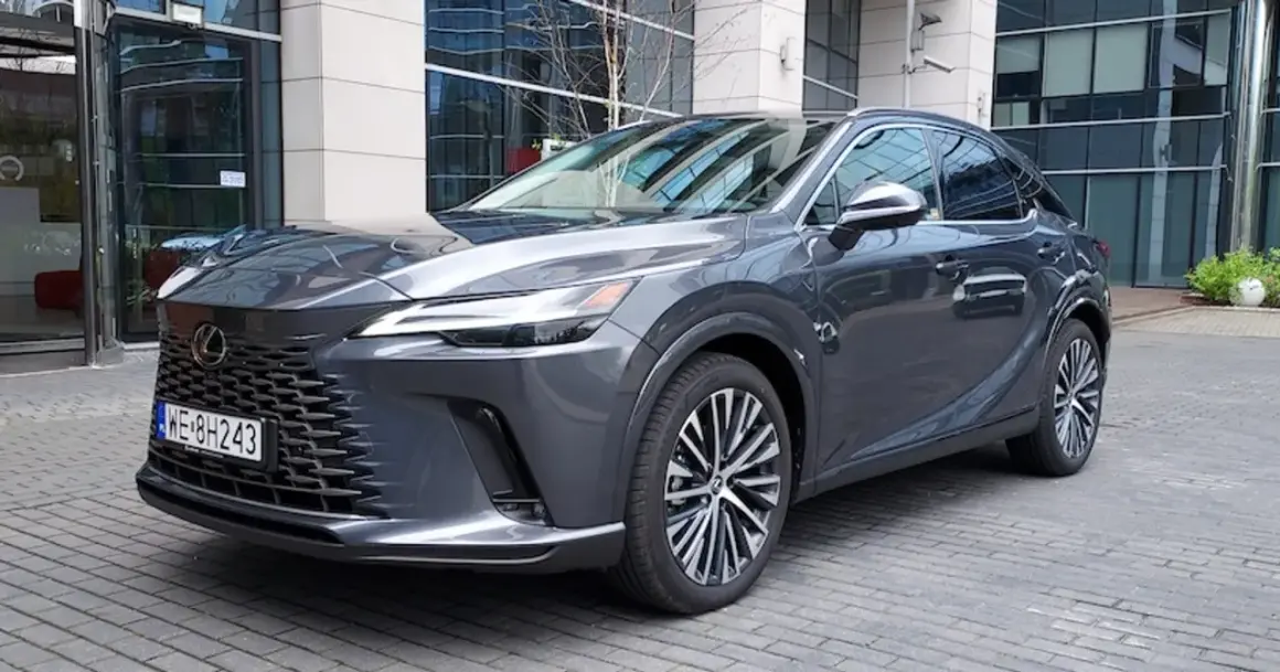 Elegancki, ciemnoszary Lexus RX 450h z nowoczesnym grillem i felgami stoi przed budynkiem biurowym.