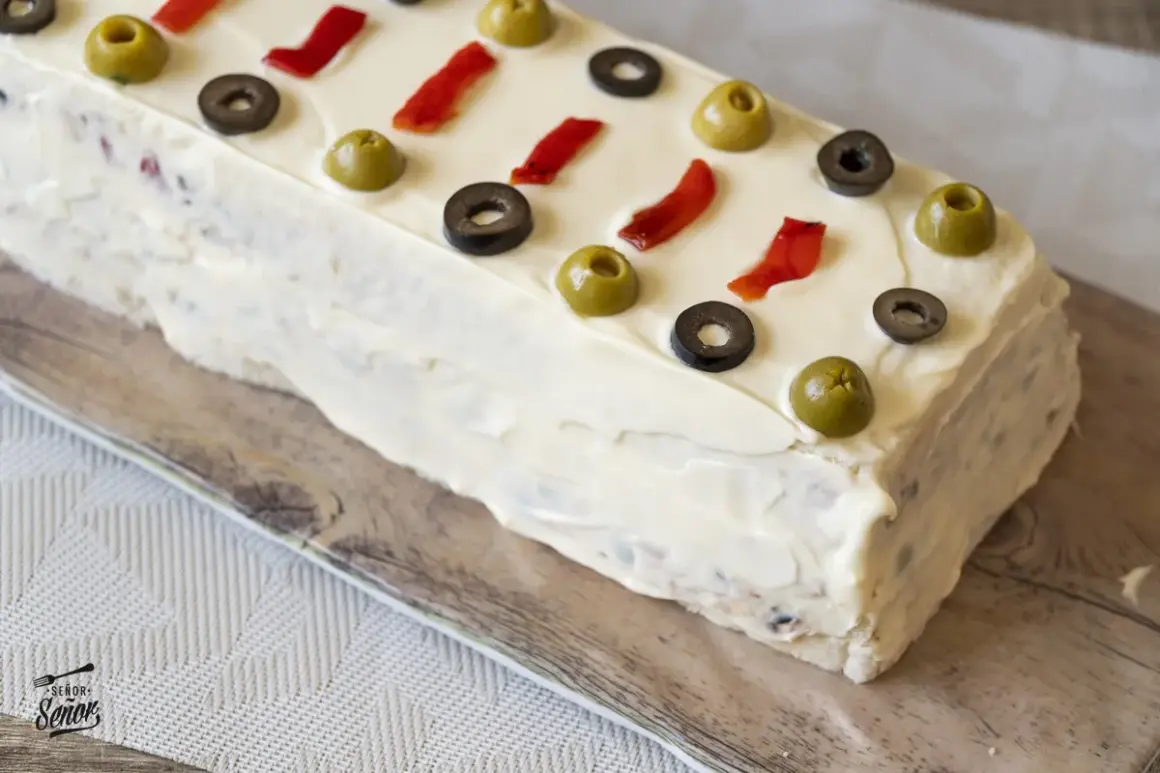 Pastel frío de atún decorado con aceitunas y pimientos rojos.
