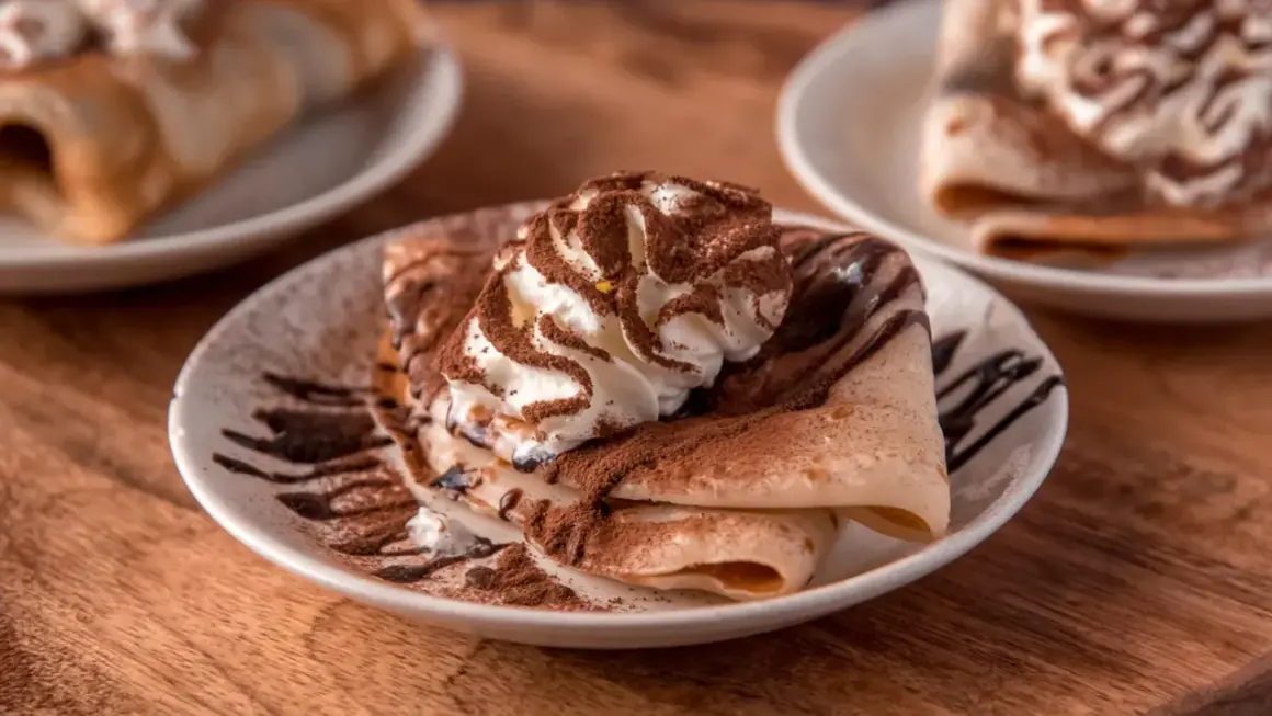 Deliziose crepes senza uova, guarnite con panna montata, cacao e sciroppo al cioccolato, un piacere per gli occhi e il palato.