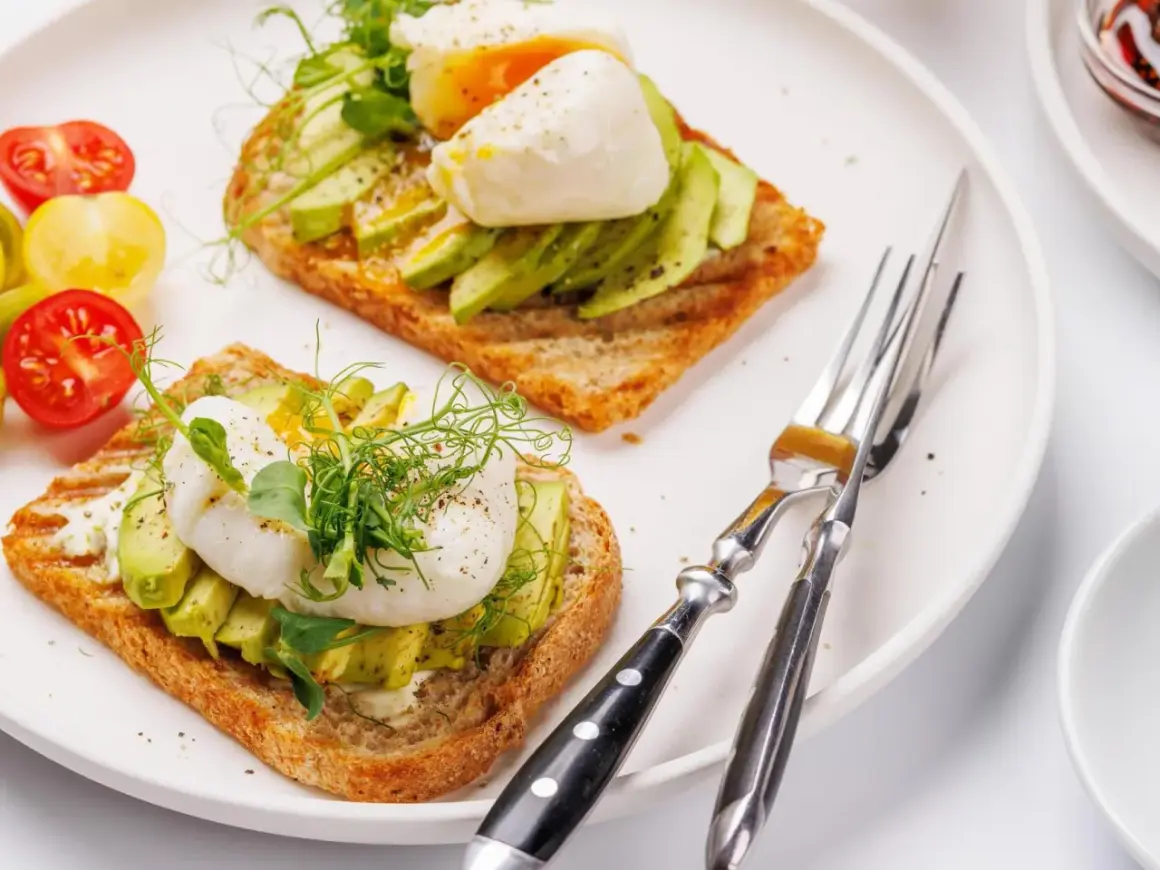 Zwei Scheiben Toast mit Avocado und pochiertem Ei, garniert mit Sprossen. Ein köstliches Egg Benedict Avocado Gericht.