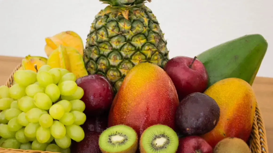 Koszyk pełen owoców: ananas, mango, winogrona, jabłka, śliwki, kiwi, awokado i karambola. Naturalna fruktoza w najlepszym wydaniu.