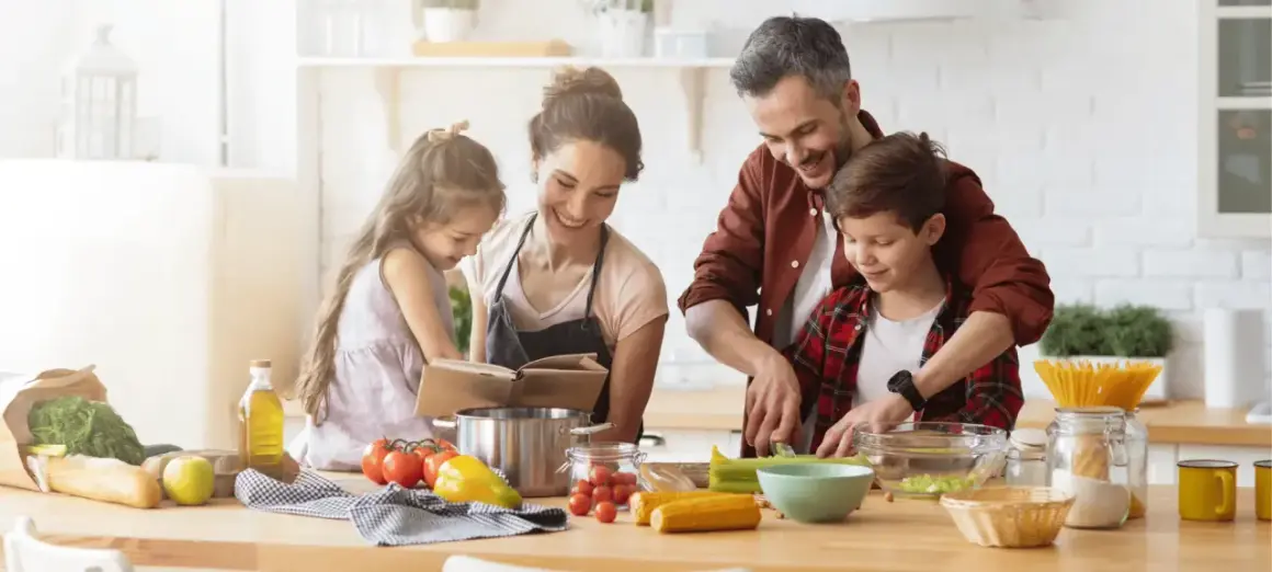 Famille préparant un repas. Le père aide son fils à couper des légumes. La mère et la fille consultent un livre de recettes. On se demande : lactose c'est quoi ?