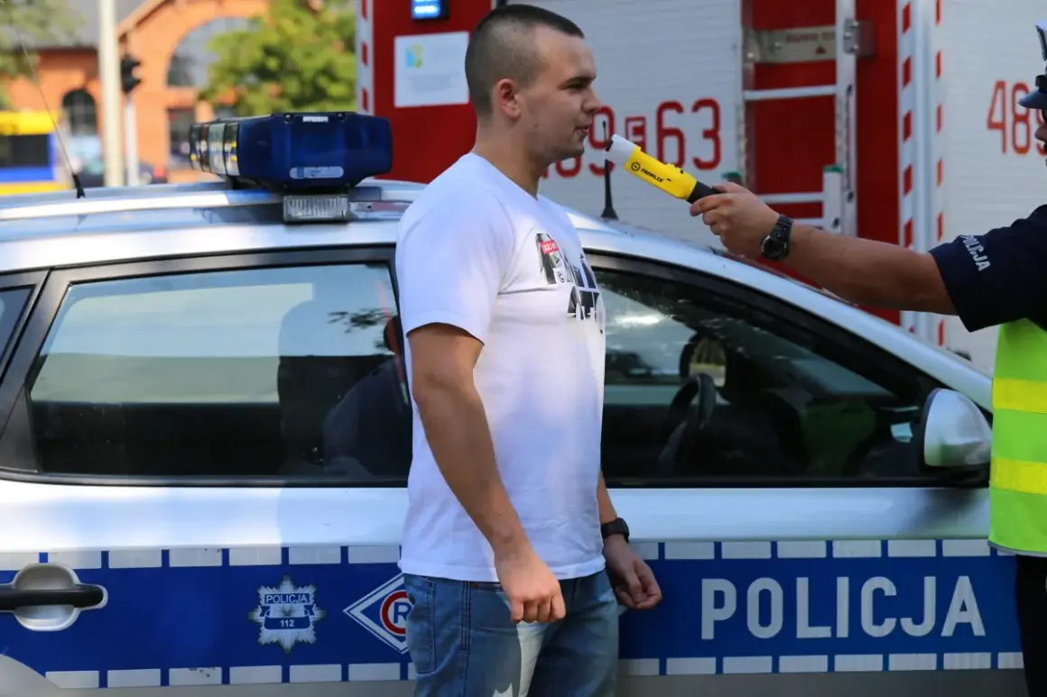 Policjant bada alkomatem mężczyznę obok radiowozu.