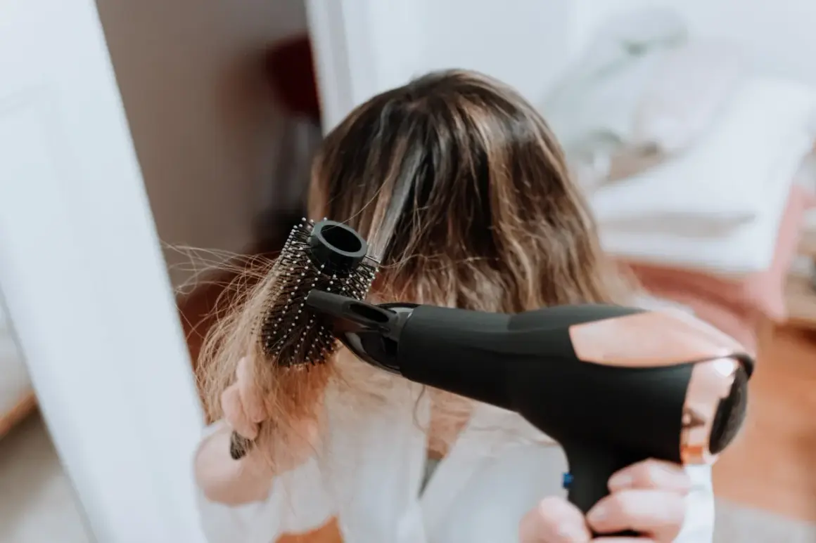Frau föhnt ihre Haare mit einer Rundbürste, um fliegende Haare zu bändigen.