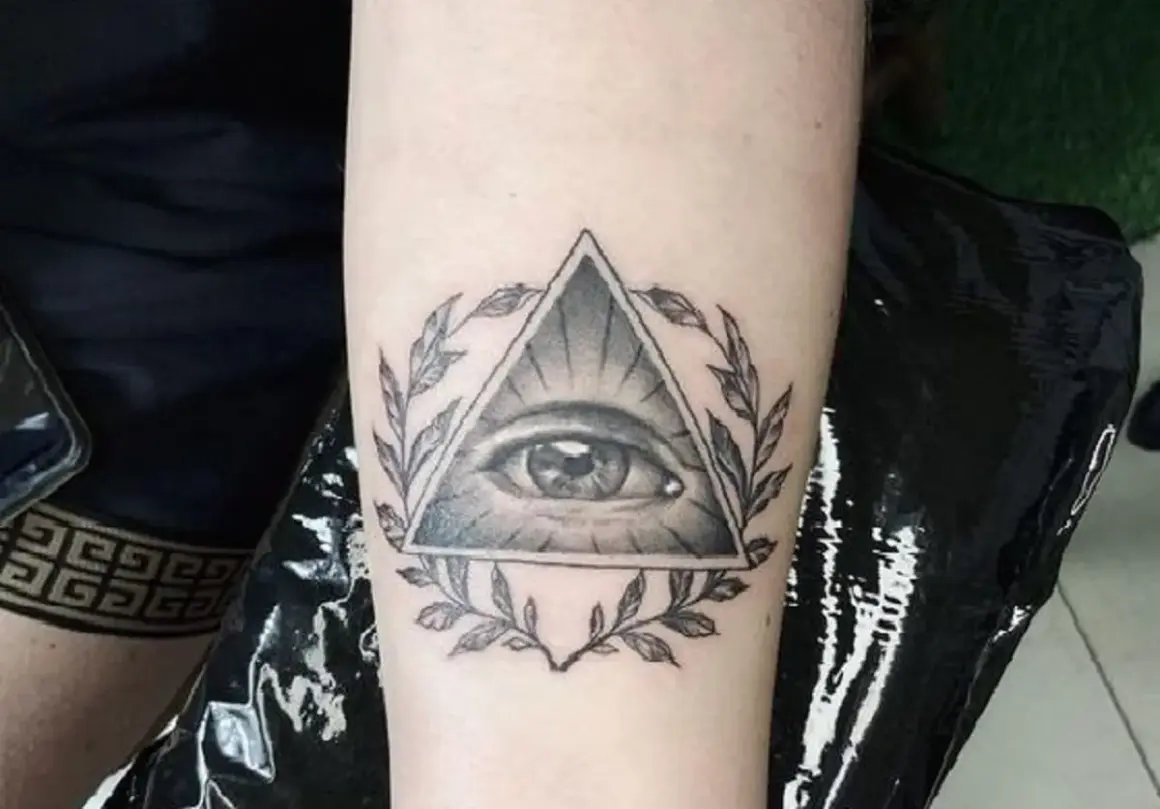 Oko proroka tatuaz w trójkącie otoczone gałązkami. Symbol czujności i wiedzy.