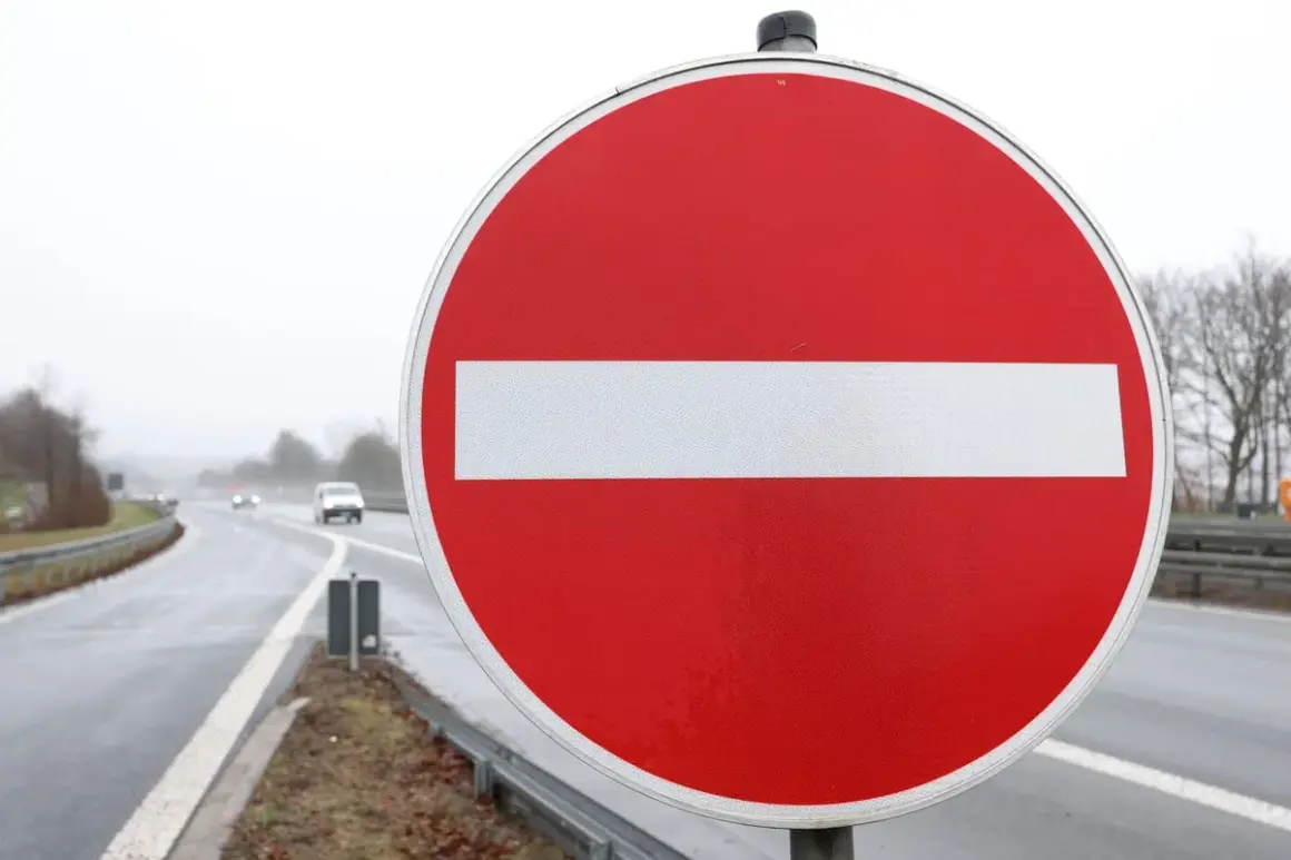 Ein rotes Rundschild mit weißem Balken: durchfahrt verboten schild. Autos fahren auf nasser Straße im Hintergrund.