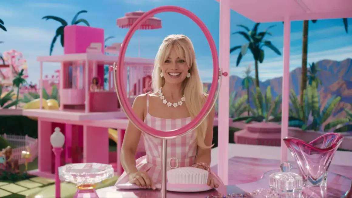 Margot Robbie als Barbie in ihrem pinken Traumhaus, lächelnd durch einen Spiegel.