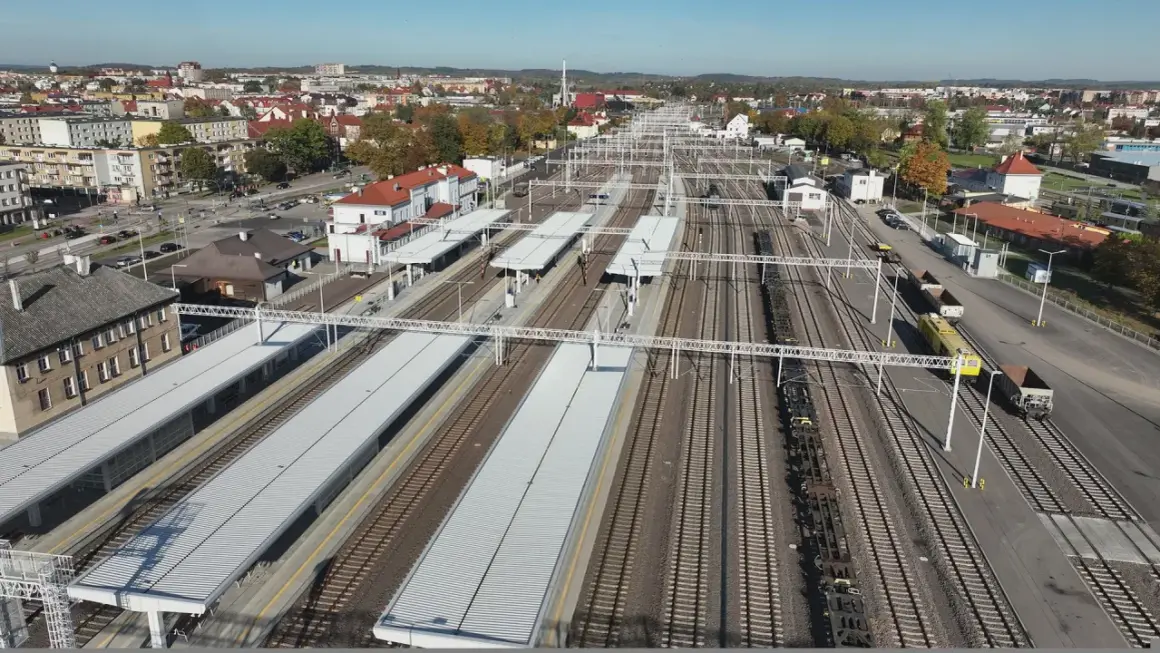 Widok z lotu ptaka na dworzec PKP Ełk z licznymi torami, peronami i budynkami. W oddali widać miasto.