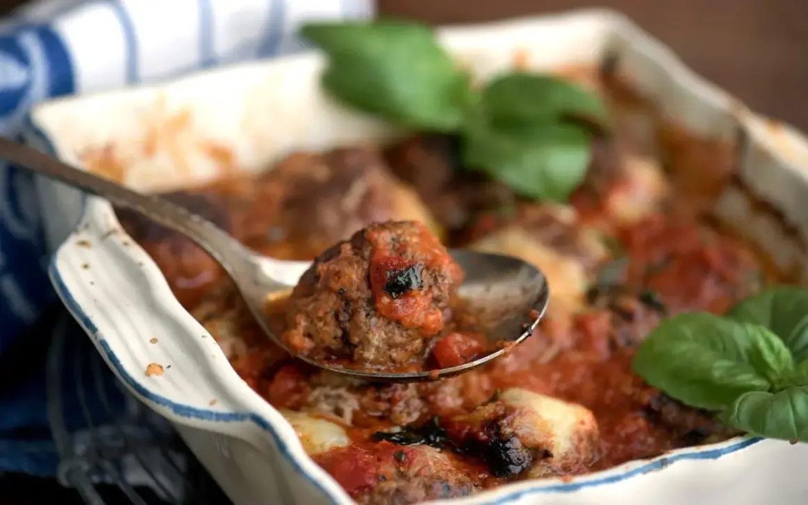 En sked lyfter en köttbulle täckt av mustig tomatsås ur en ugnsform. En härlig pasta med tomatsås väntar!