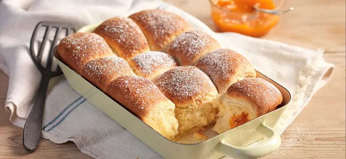 Frisch gebackene Buchteln, bestäubt mit Puderzucker, warten darauf, mit Marillenmarmelade gefüllt zu werden. Ein echtes Buchteln original Rezept.
