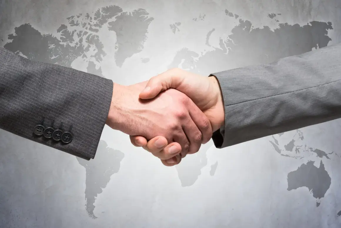 Uścisk dłoni dwóch mężczyzn w garniturach na tle mapy świata. Symbolizuje globalne partnerstwo i ddp.