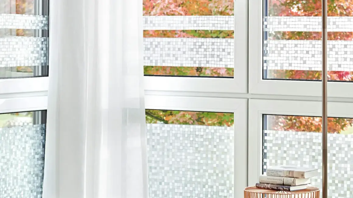 Fenster mit statischer Fensterfolie im Mosaikmuster, die Privatsphäre schafft. Ein weißer Vorhang hängt daneben.