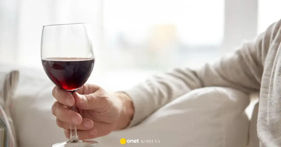 Dłoń trzyma kieliszek czerwonego wina. Czy czerwone wino obniża ciśnienie? Warto to sprawdzić.