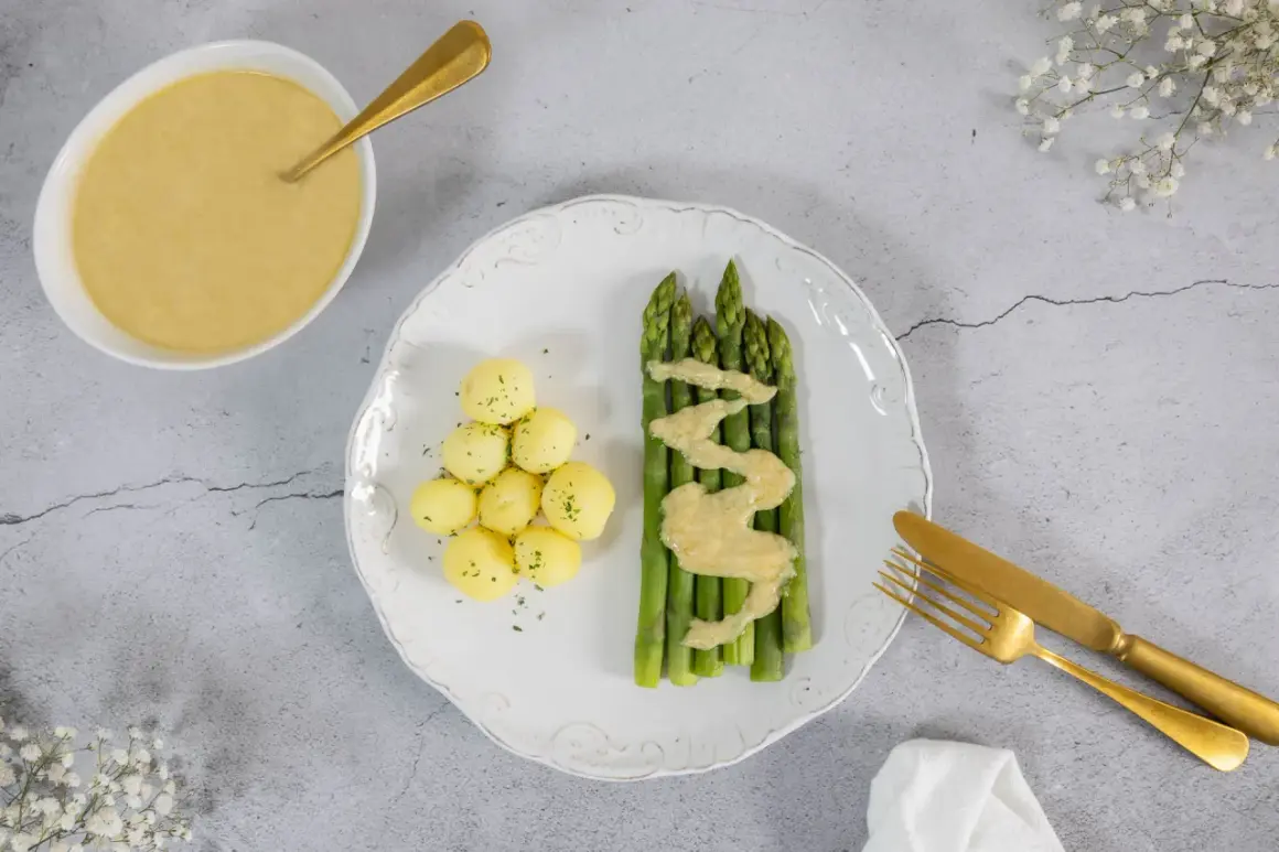 Spargel mit kleinen Kartoffeln und einer cremigen, veganen Sauce Hollandaise. Ein goldener Löffel liegt bereit.