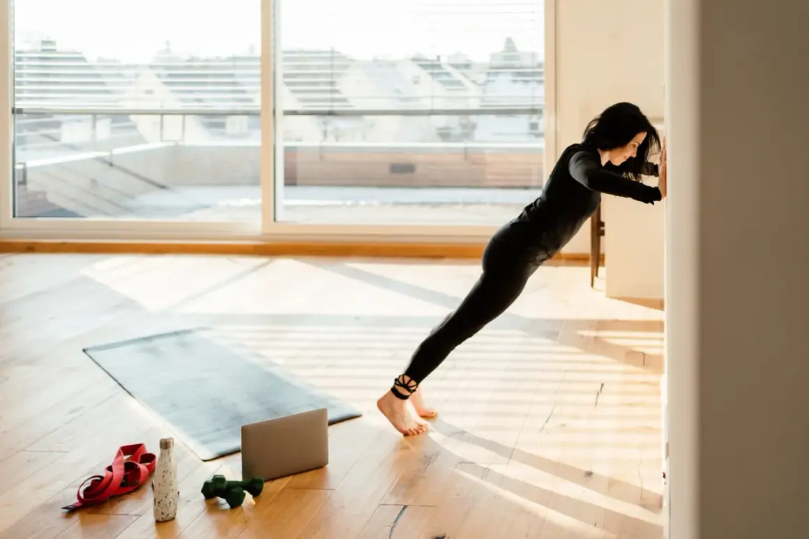 Frau macht Liegestütze an der Wand, um zu lernen, wie trainiert man. Trainingsmatte, Hanteln und Wasserflasche liegen bereit.