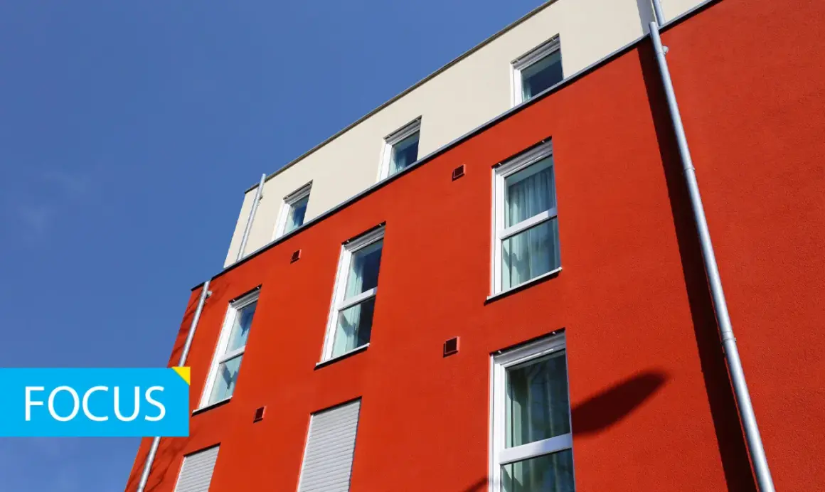 Edificio moderno con facciata rossa e intonaco graffiato per esterni. Finestre bianche e cielo blu.
