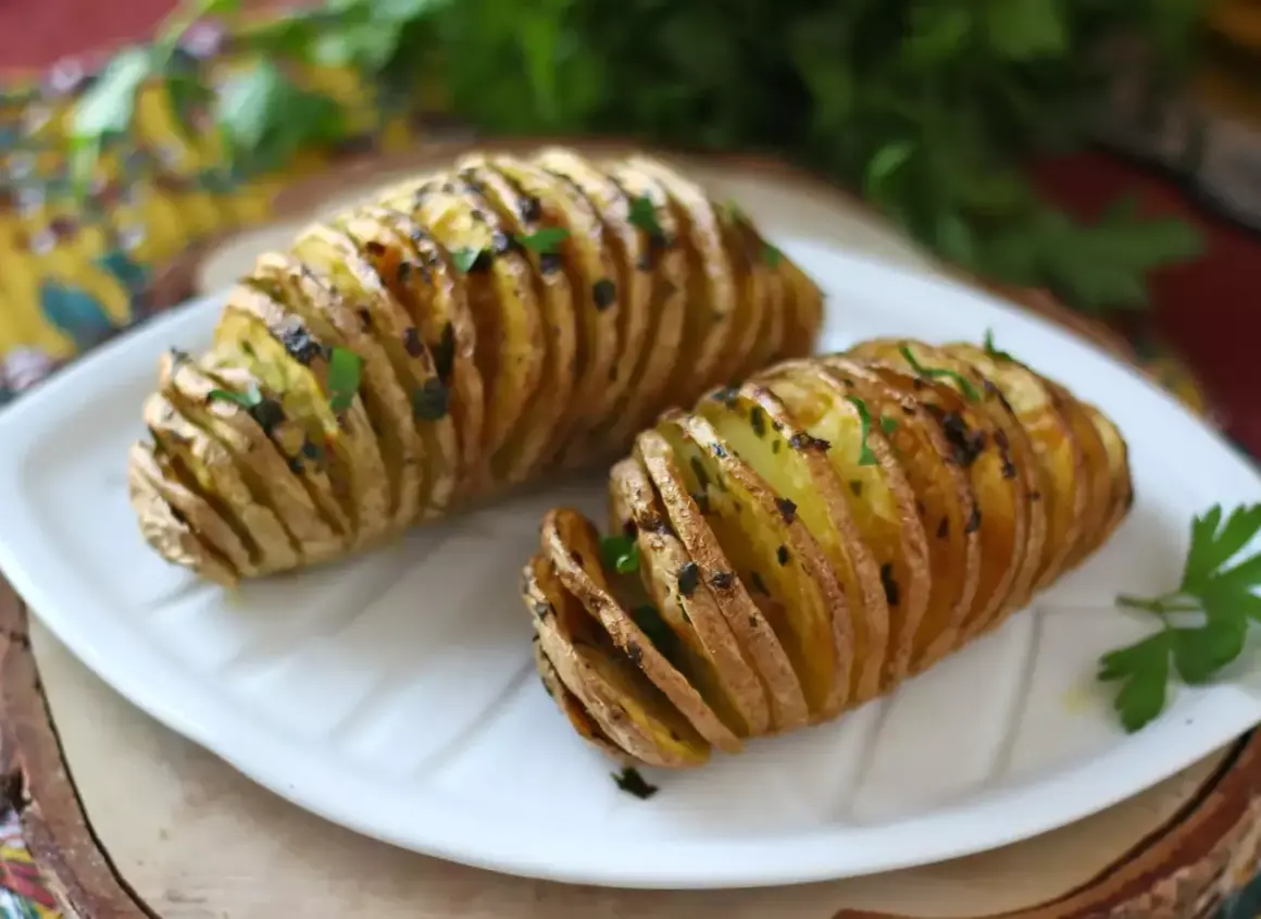 Två gyllene hasselbackspotatis med parmesan och färska örter på en vit tallrik.