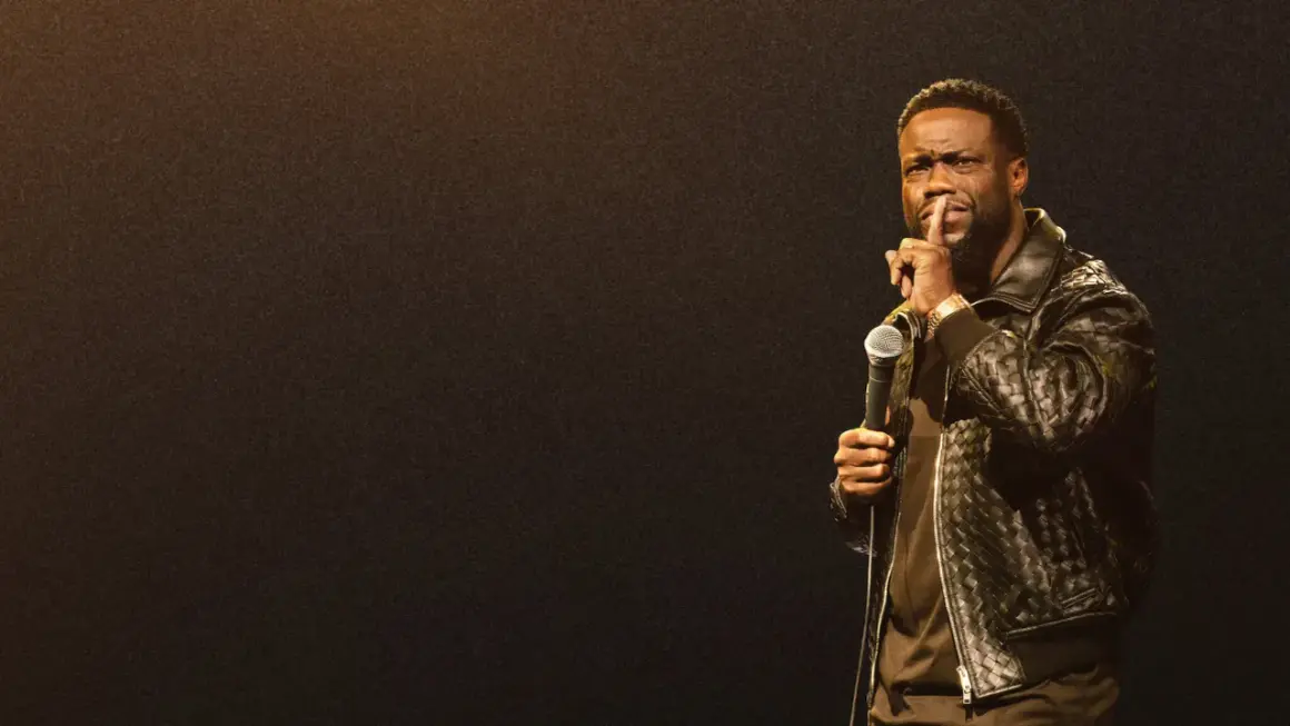 Kevin Hart stand up, trzymając mikrofon i gestykulując do publiczności.