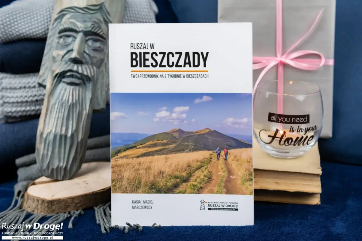 Książki o Bieszczadach zachęcają do podróży. Na okładce przewodnik po Bieszczadach, obok rzeźba i świeca.