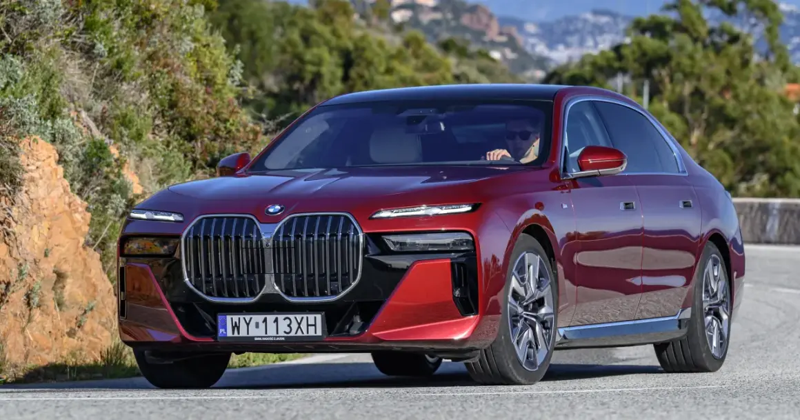 Czerwone BMW serii 7 z kierowcą za kierownicą, jadące po krętej drodze.