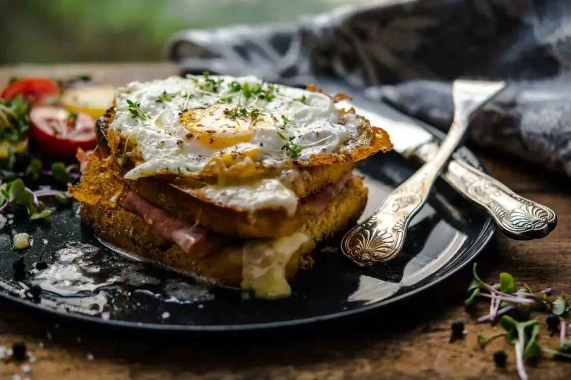 Ein üppiger Croque Monsieur mit Spiegelei, Schinken und geschmolzenem Käse, garniert mit Kräutern und Beilagen.