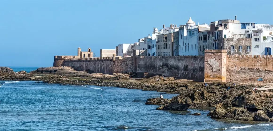 Vue des remparts d'Essaouira, avec des maisons blanches en arrière-plan. Les rochers et la mer invitent à toutes les activités.