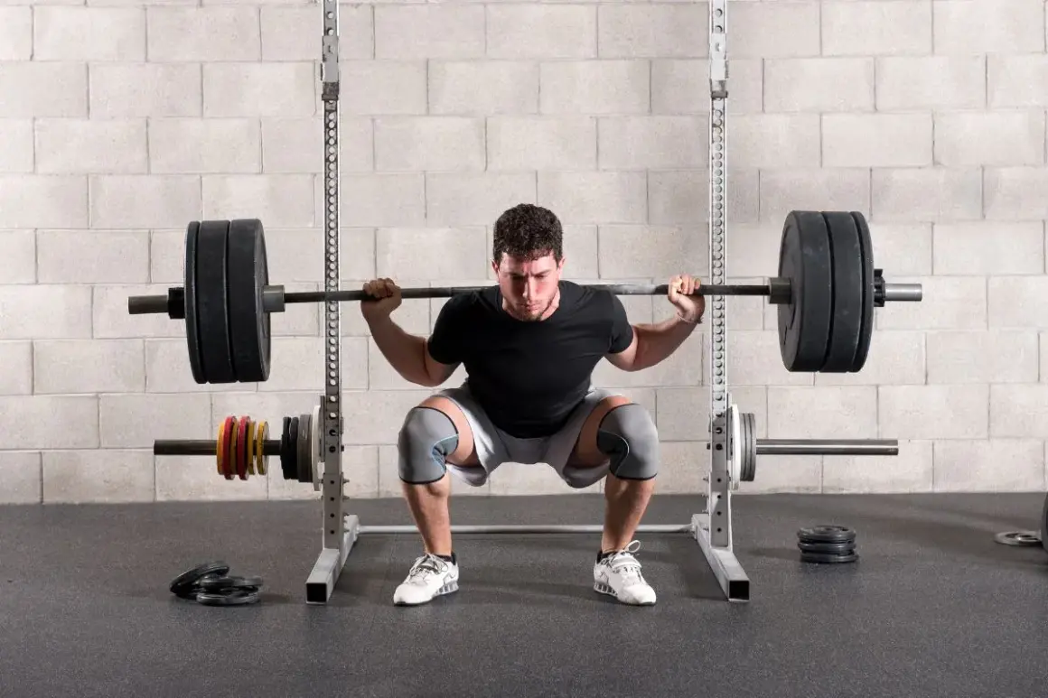 Un homme concentré effectue un back squat, la barre chargée reposant sur ses épaules, dans une salle de sport.
