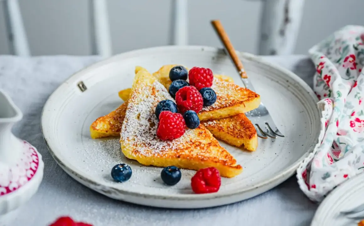 Goldbraune French Toast-Scheiben, bestäubt mit Puderzucker und garniert mit frischen Beeren. Ein perfektes Frühstück, das Lust auf mehr macht.