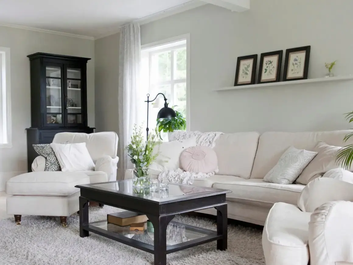 Gemütliches Wohnzimmer mit einem Sofa und Sessel in off white farbe, einem schwarzen Schrank und einem Couchtisch.