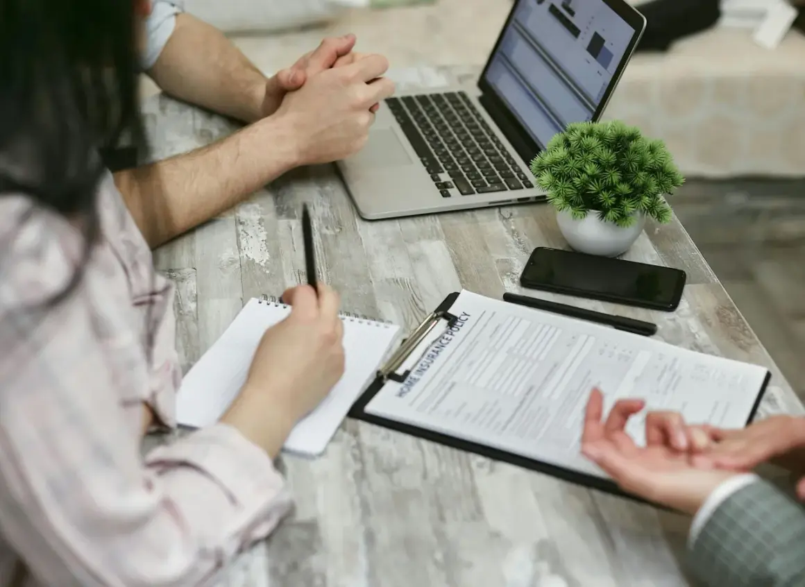 Osoby przy stole analizują dokument "Home Insurance Policy". Kobieta notuje, mężczyzna patrzy na laptopa. Może to być związane z wefox wypowiedzenie oc.