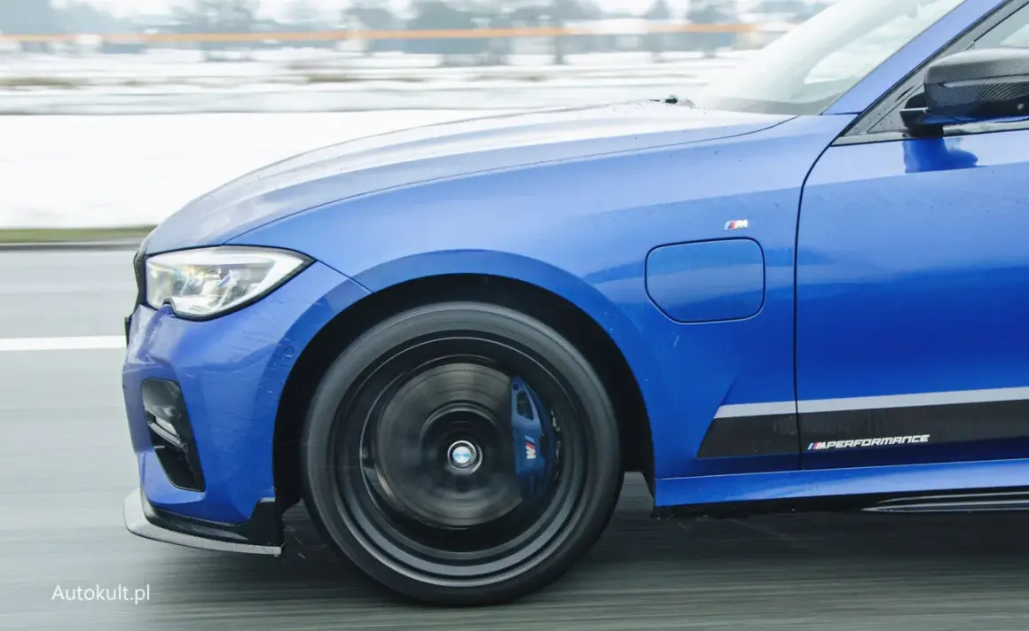 Niebieskie BMW 330e z napisem M Performance na progu, w ruchu drogowym.