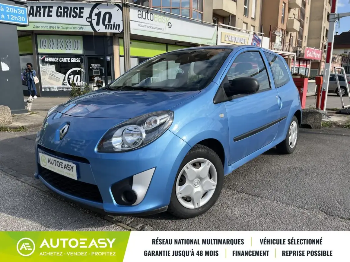 Une Twingo 2 phase 2 bleue, garée devant un commerce.