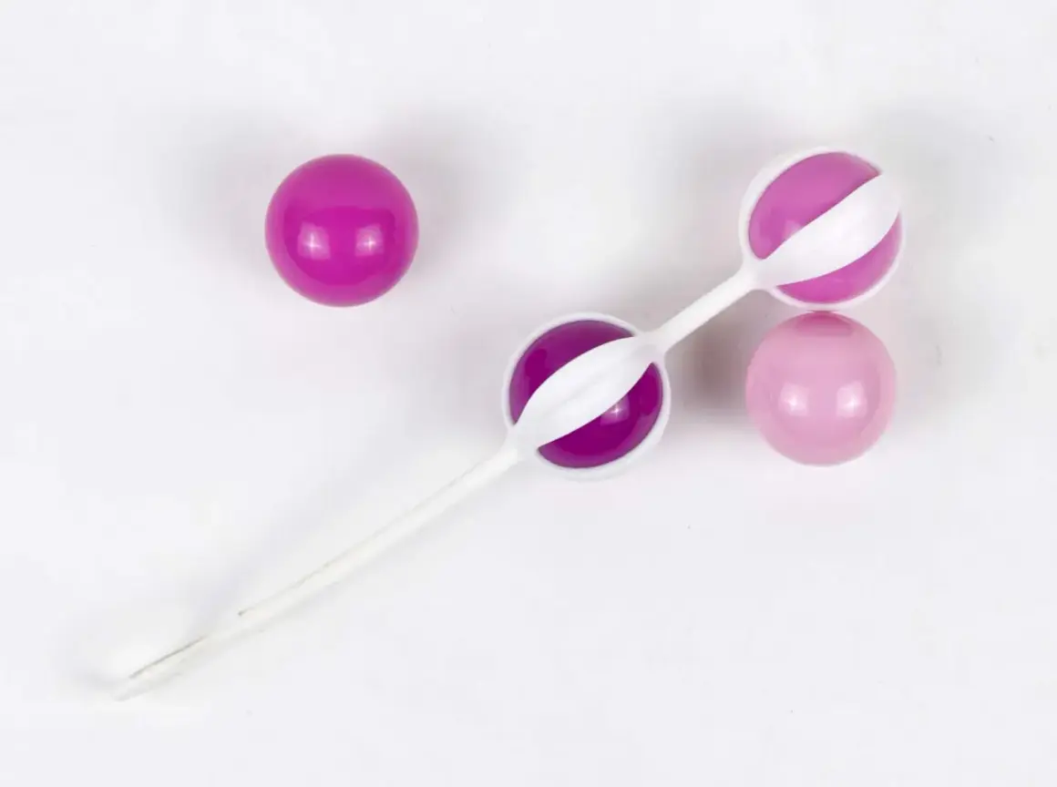 Trois boules de geisha, deux roses et une violette, sur fond blanc.