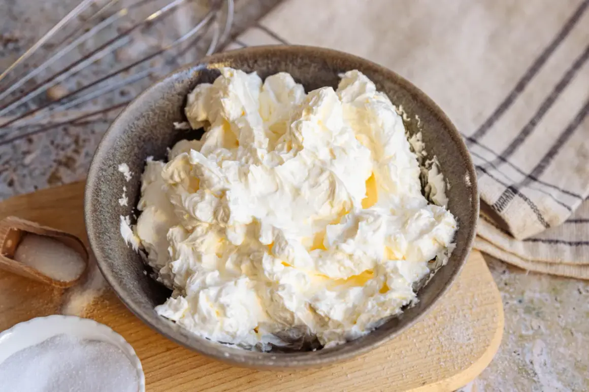 Schüssel mit luftiger, weißer italienischer Buttercreme, bereit für süße Kreationen. Daneben Zucker und ein Schneebesen.