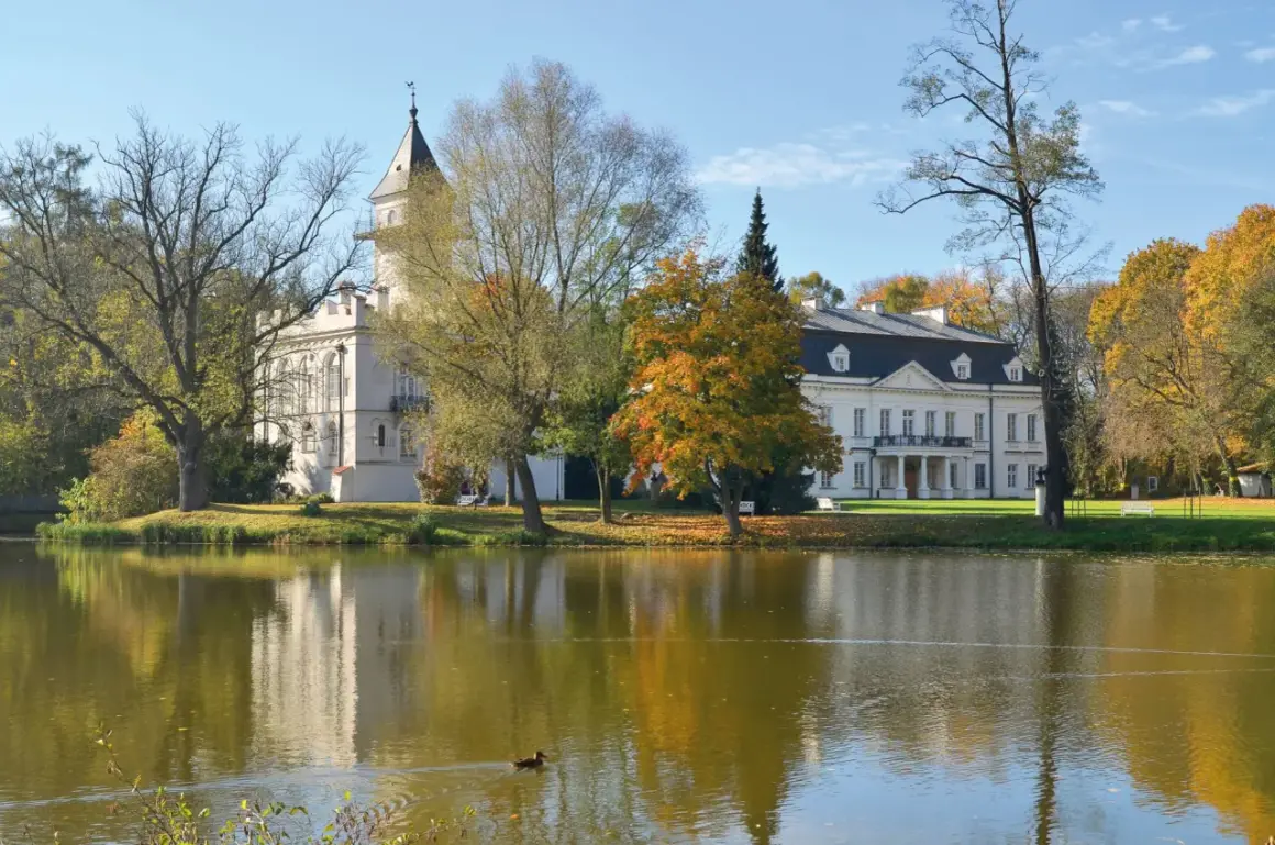 Pałac w jesiennej scenerii nad jeziorem, część Bolimowskiego Parku Krajobrazowego. Kaczka pływa po wodzie.