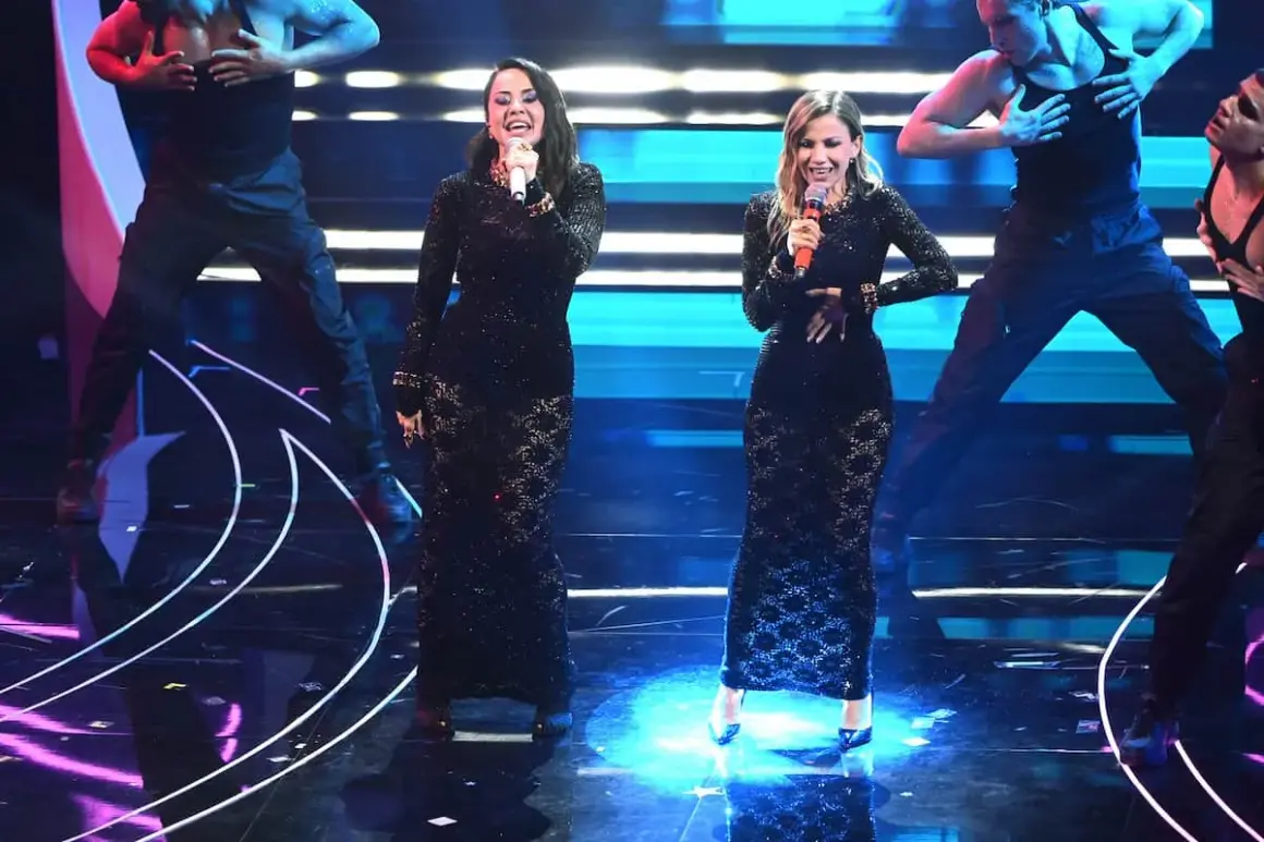 Due sorelle cantanti italiane, vestite con abiti neri scintillanti, si esibiscono sul palco con ballerini sullo sfondo.