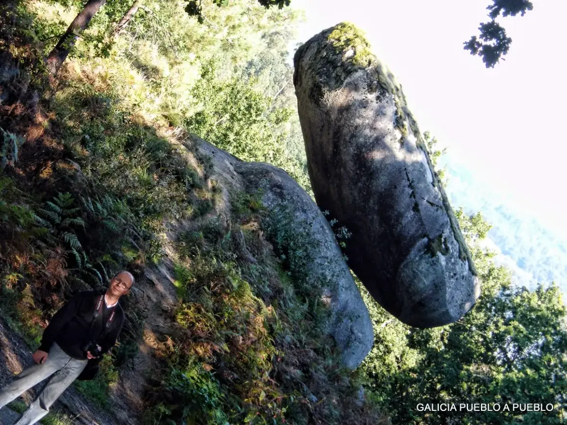 Hombre sonriente junto a una roca suspendida, un ejemplo de la pena do equilibrio en la naturaleza.