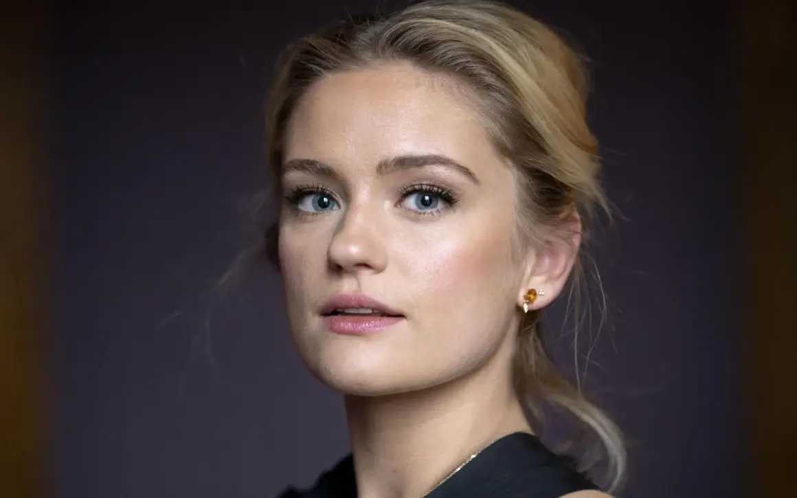 Alicia Agneson, med blå ögon och blont hår uppsatt i en hästsvans, bär en guldig örhänge.