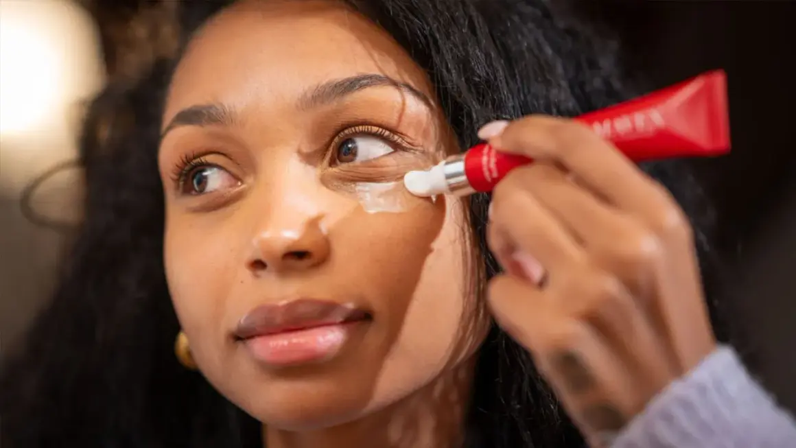 Donna applica crema contorno occhi per contrastare i segni sotto gli occhi, con un tubetto rosso.