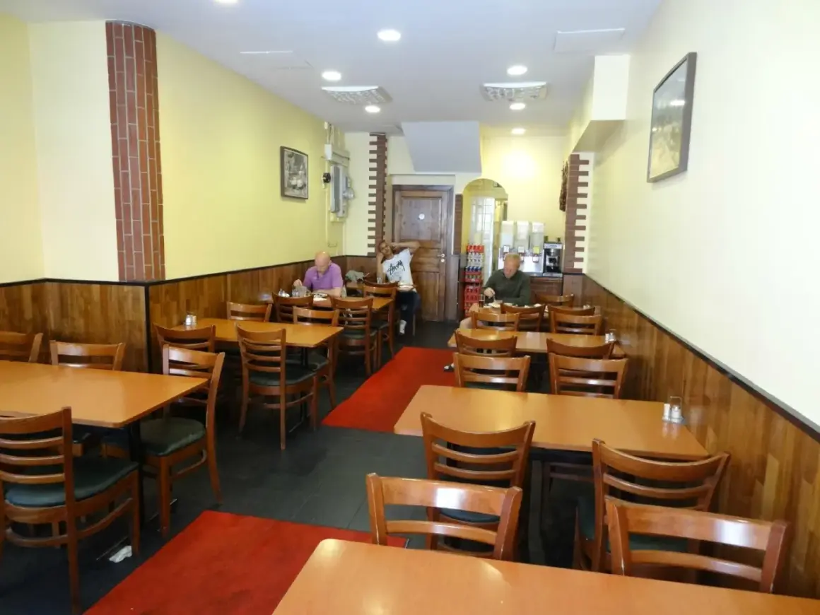 Interiör av en turkisk restaurang i Stockholm. Flera bord med trästolar och röda mattor. Tre gäster sitter vid borden.