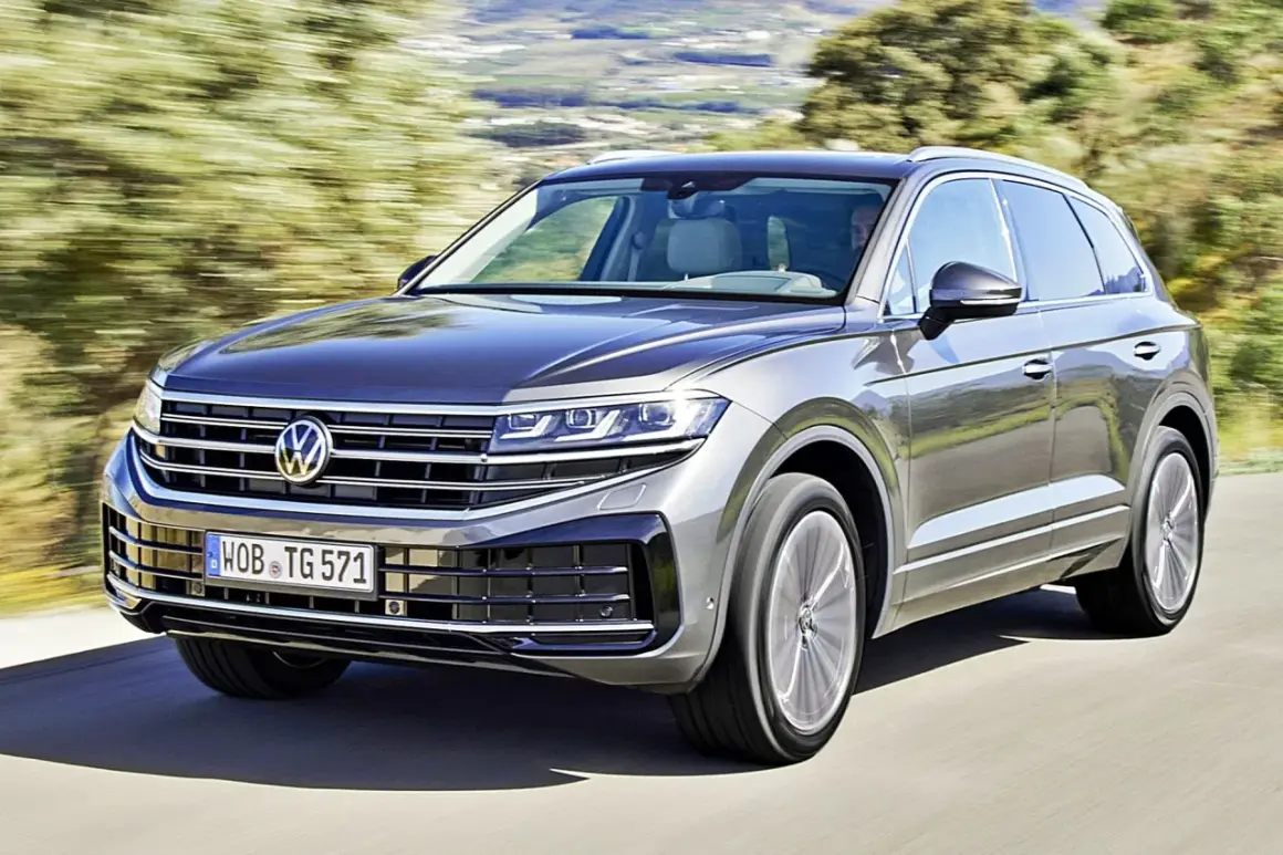 Szary Volkswagen Touareg pędzi po drodze, otoczony zielenią.