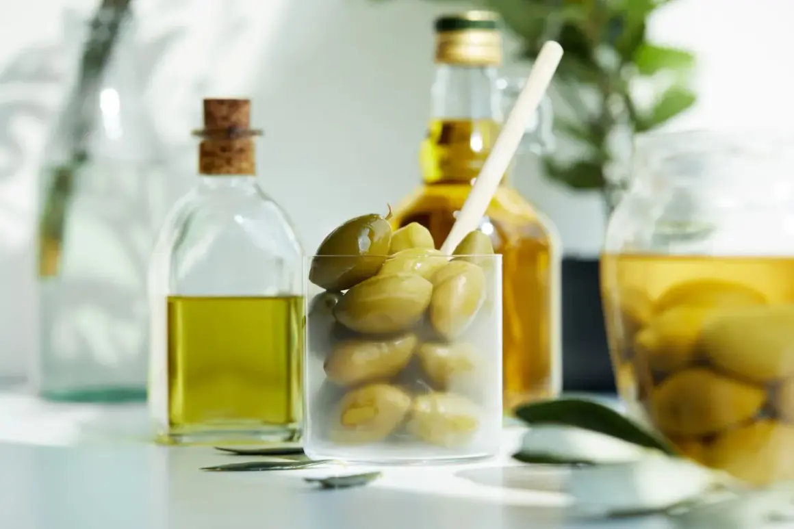 Zielone oliwki w szklance, obok butelki oliwy. Zastanawiasz się nad oliwki kcal?