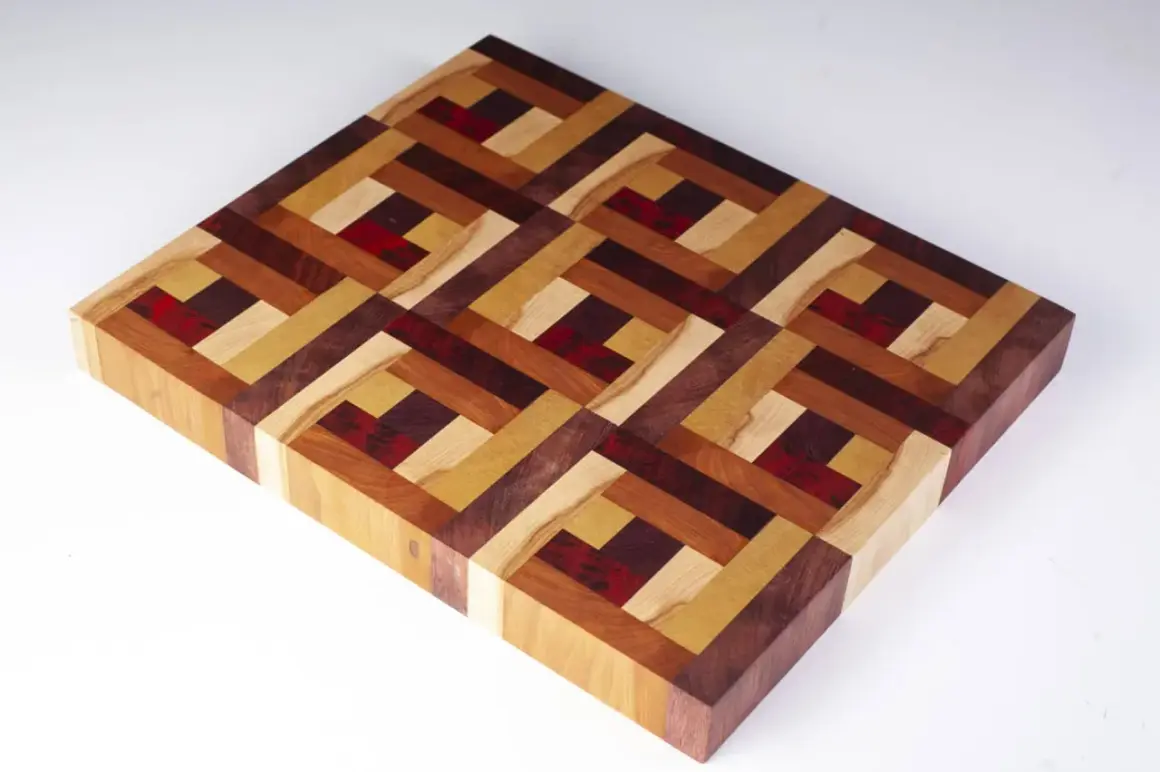 A beautiful diy cutting board with an intricate geometric pattern made from various wood types and red accents.